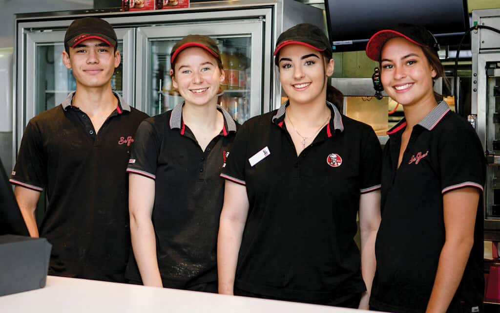 Four KFC workers are standing behind the counter smiling.