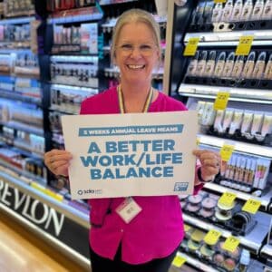 An SDA member in Priceline is holding up a sign that says a better work/life balance. They are smiling.